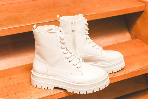 White demi-season boots made of eco-leather with fasteners, laces and rough soles stand on wooden steps, close-up side view. The concept of fashion and women's shoes. - Foto, immagini