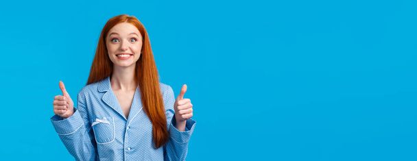Cheerful and excited redhead girl cant wait try out, agree with temptation and interest, showing thumbs-up smiling thrilled and enthusiastic nod with approval, like idea, standing blue background. - Photo, Image