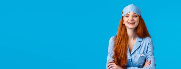 Assertive and confident good-looking optimistic redhead girl ready go bed, wearing sleep mask and cute nightwear, hold hands crossed chest like professional, self-assured pose, blue background. - Photo, Image