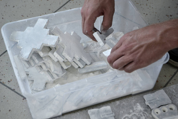 Mannelijke werknemer sorteert door modellen in handen, liggend in doos en bedekt met wit polyamide poeder close-up. Objecten gedrukt op poeder 3D printer. Technologie Multi Jet Fusion MJF. 3D-printtechnologie - Foto, afbeelding