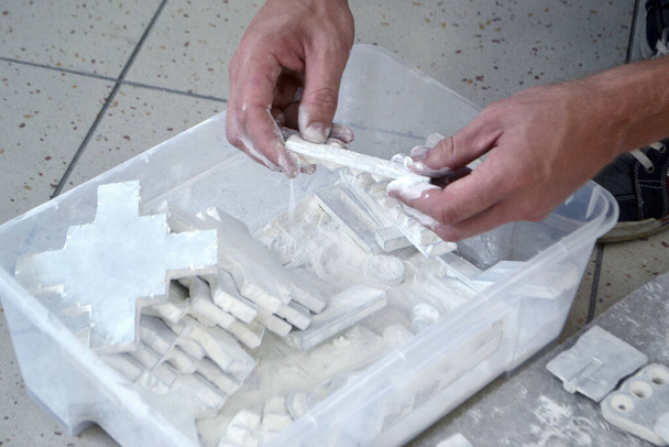Mannelijke werknemer sorteert door modellen in handen, liggend in doos en bedekt met wit polyamide poeder close-up. Objecten gedrukt op poeder 3D printer. Technologie Multi Jet Fusion MJF. 3D-printtechnologie - Foto, afbeelding