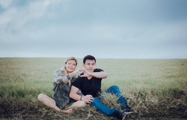 Coppia seduta sull'erba facendo una forma di cuore con le mani. Giovane coppia innamorata nel campo rendendo la forma del cuore. Gli amanti seduti sul campo a fare una forma di cuore con le mani - Foto, immagini