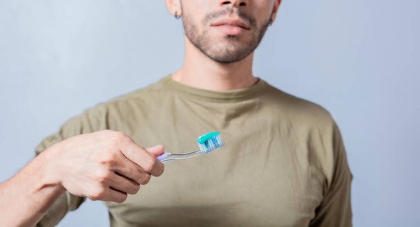 Kerl mit unkenntlichem Gesicht hält Bürste mit Zahnpasta auf isoliertem Hintergrund, zeigt Zahnbürste - Foto, Bild