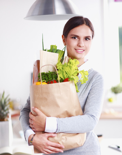 Young woman holding grocery shopping bag with vegetables Standing in the kitchen. - 写真・画像