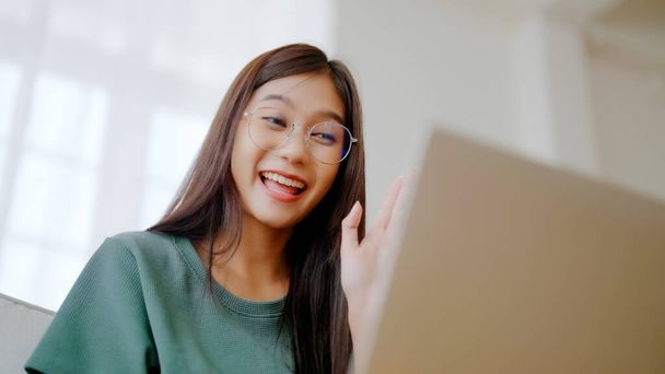 Lächelnde junge Asiatin, die zu Hause am Laptop arbeitet. Attraktive Asiatinnen mit Computerfernstudium, Online-Bildung und Videotelefonie - Foto, Bild