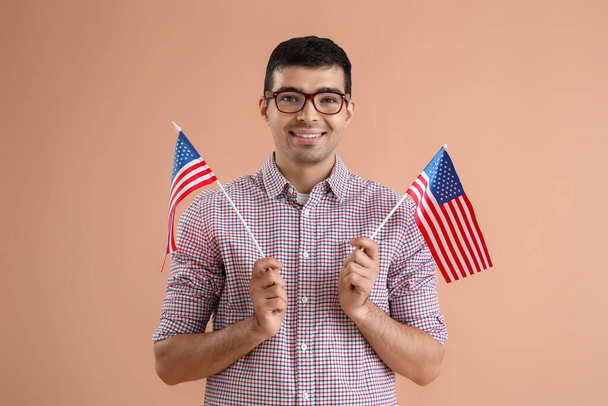Bej arka planda ABD bayrakları olan gözlüklü genç bir adam. - Fotoğraf, Görsel