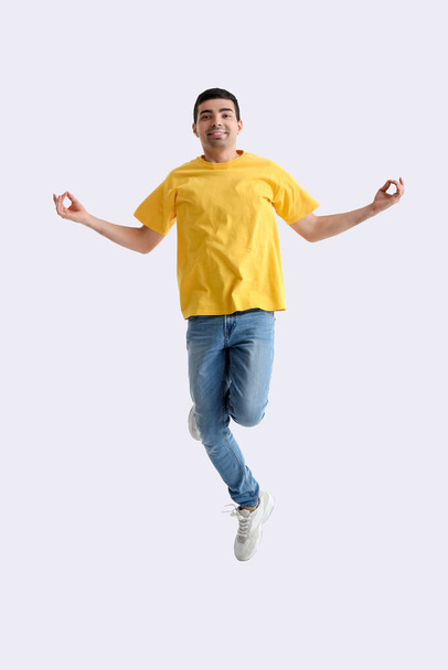 Jongeman in geel t-shirt mediteren tijdens het springen op lichte achtergrond - Foto, afbeelding