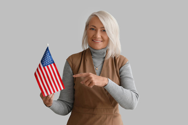 Kypsä nainen osoittaa Yhdysvaltain lipun harmaalla taustalla - Valokuva, kuva