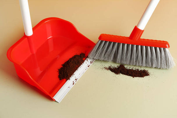 Cleaning of scattered coffee with dustpan and broom on color background, closeup - Photo, Image