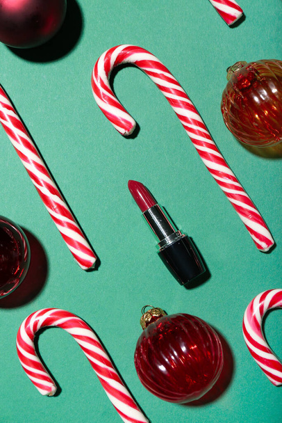緑の背景に赤い口紅、キャンディーの杖とクリスマスボールと組成物 - 写真・画像
