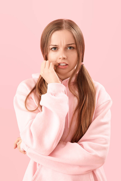 Mujer joven en sudadera con capucha mordiendo las uñas sobre fondo rosa, primer plano - Foto, imagen