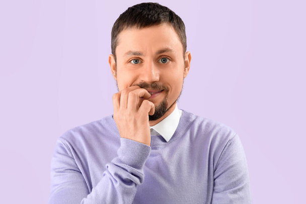 Bonito homem mordendo unhas no fundo lilás, close-up - Foto, Imagem