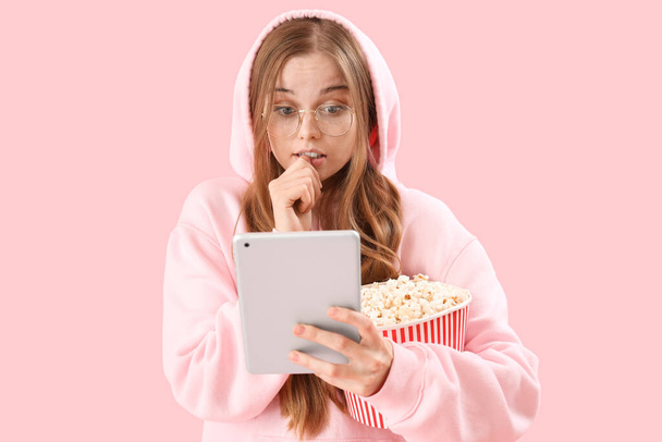 fiatal nő tabletta számítógép és popcorn harapás körmök rózsaszín háttér - Fotó, kép
