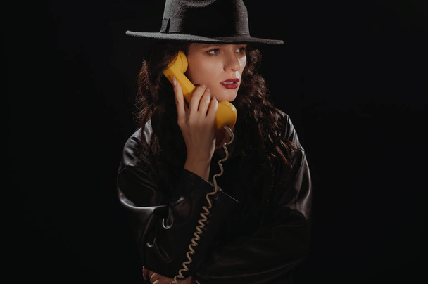 Dark noir portrait of a female detective holding a retro telephone receiver. Private detective, spy, investigation concept - Photo, image
