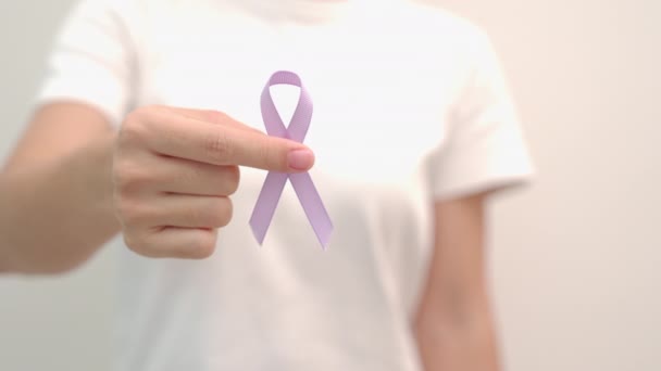 Día Mundial del Cáncer, 4 de febrero. Mano de mujer sosteniendo la cinta púrpura lavanda para apoyar a las personas que viven y enferman. Salud y concepto médico - Metraje, vídeo