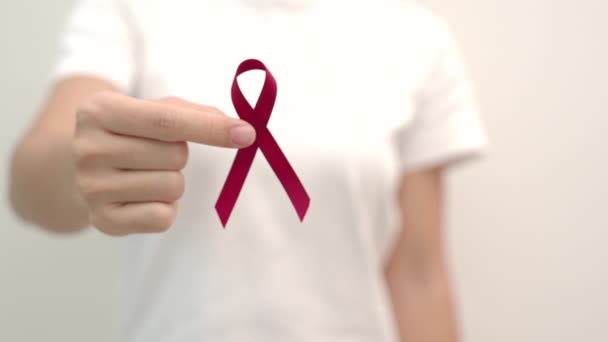 Hand hält rotes Band zum Welt-Aids-Tag im Dezember, zum Monat des Bewusstseins für Multiples Myelom und zur Nationalen Woche des Roten Bandes. Konzept zum Gesundheits- und Weltkrebstag - Filmmaterial, Video