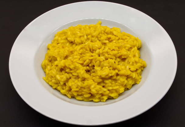 Italiano Risotto allo Zafferano (arroz com açafrão) em um prato branco isolado em fundo preto - Foto, Imagem