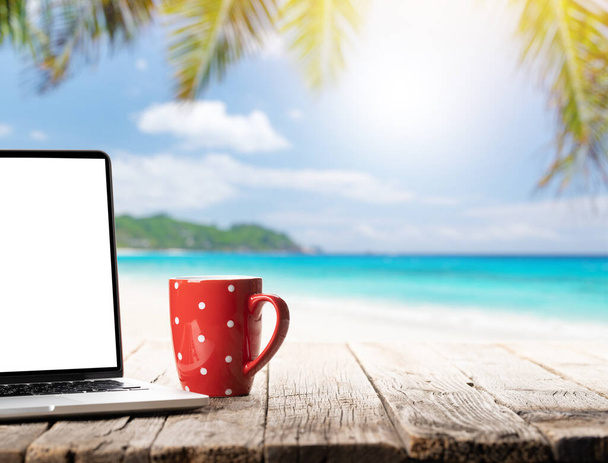 Laptop ve kahve fincanı güneşli denizin ve palmiye yapraklarının önündeki ahşap masada. İş ve seyahat ya da uzak iş konsepti - Fotoğraf, Görsel