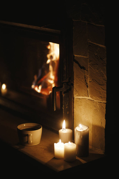 Caliente taza de té y velas en la acogedora chimenea en la sala de noche oscura. Chimenea calefacción en casa, apagón eléctrico. Tiempo atmosférico en la chimenea en casa - Foto, Imagen