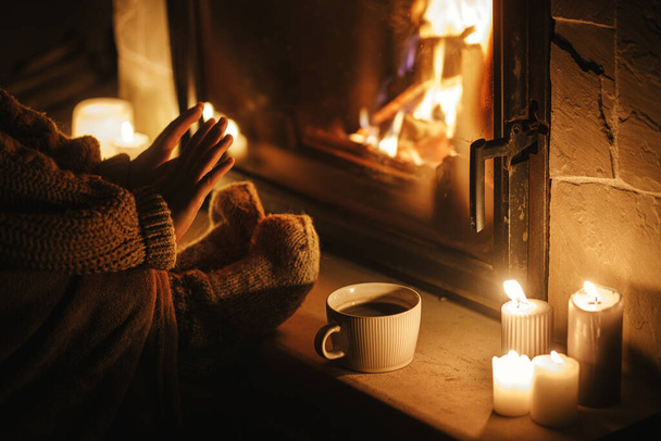Stilvolle Frau wärmt Hände und Füße am gemütlichen Kamin mit Tee am Abend. Kaminheizung im Haus, Stromausfall. Stimmungsvolle Zeit am heimischen Kamin - Foto, Bild