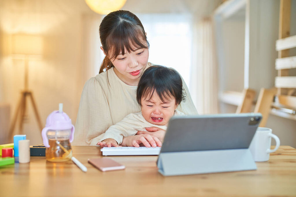 Une femme qui utilise une tablette PC et un bébé en pleurs à la maison - Photo, image