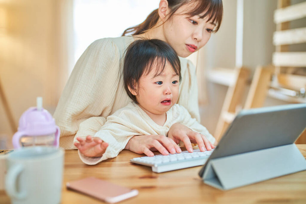 Uma mulher que opera um tablet PC e um bebê chorando em casa - Foto, Imagem
