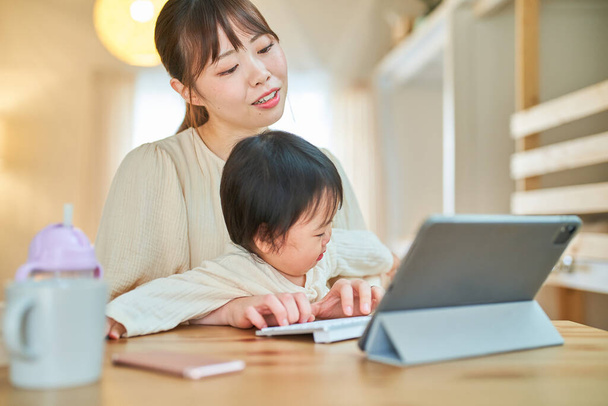 Eine Frau und ein Säugling, die zu Hause einen Tablet-PC mit müdem Gesichtsausdruck bedienen - Foto, Bild