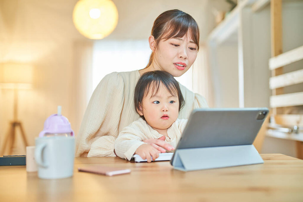 自宅で疲れた表情をしたタブレットPCを操作する女性と幼児 - 写真・画像