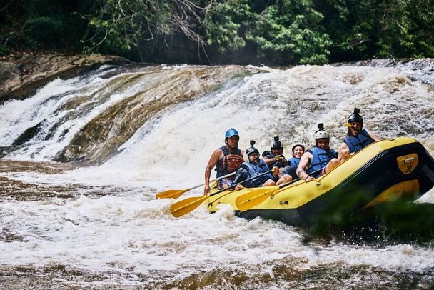We hebben het zonder al te veel moeite gedaan. een groep vastberaden jongeren op een rubberboot die overdag op sterke stroomversnellingen buiten peddelt - Foto, afbeelding