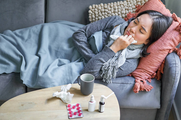 Больной грустная корейская женщина лежит на диване, чувствует себя нездоровым, простуда, грипп и температура, выглядеть расстроенным, принимать лекарства. - Фото, изображение