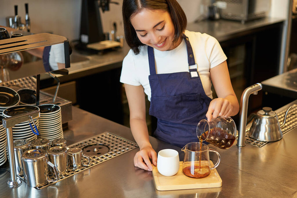 Kahvede barista, filtre kahve, tezgahın arkasında demleme ve hazırlama, mavi önlük. - Fotoğraf, Görsel