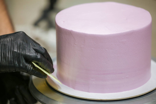 випічка шеф-кухаря з використанням шпателя і скребка згладжування вирівнювання шаруватого бузкового масляного крему матовий торт підготовка весільного торта
 - Фото, зображення