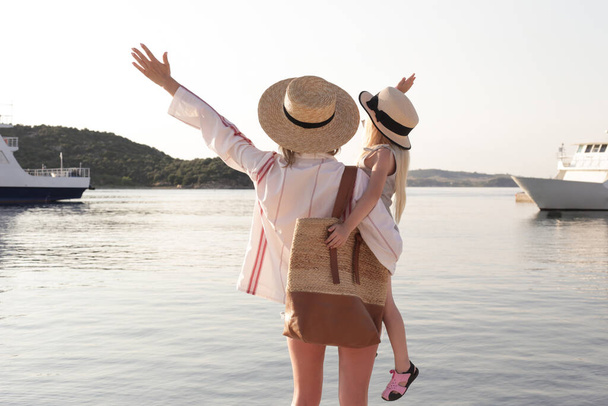 Maman et fille avec des chapeaux de paille regardant l'horizon de la mer, concept idyllique vacances d'été en famille. - Photo, image