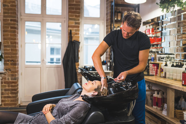 Mujer embarazada en el salón de peluquería. Peluquería masculina lavando el pelo largo de su cliente en una peluquería industrial moderna. Foto de alta calidad - Foto, imagen
