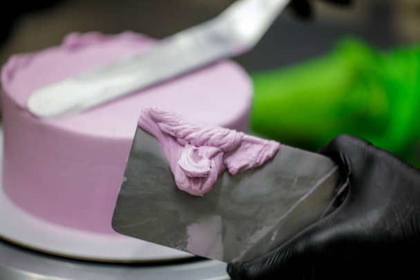 pasticciere utilizzando spatola raschietto per lilla crema di burro rosa torta glassata preparazione torta di compleanno - Foto, immagini