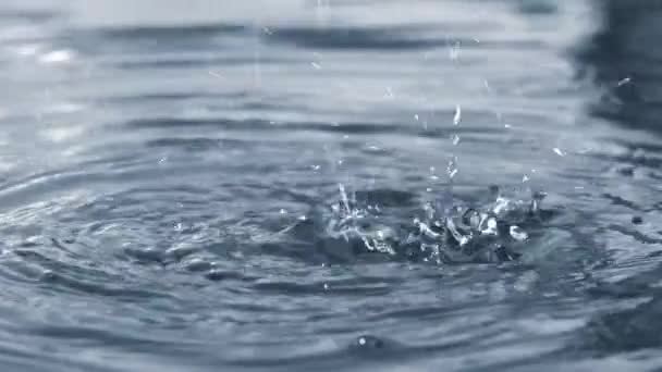 Gyönyörű cseppek és vízfolyások hullanak a szökőkút kék tiszta vizébe. Cseppek és körök a vízen közelről Full HD lassított videó. - Felvétel, videó