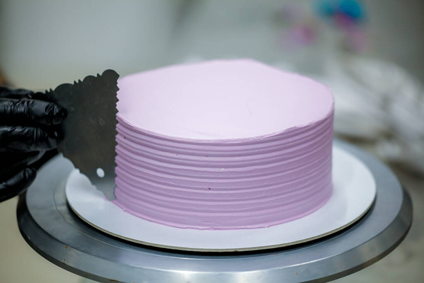 chef pâtissier utilisant grattoir spatule pour lisser lilas rose beurre crème gâteau givré - préparation gâteau d'anniversaire - Photo, image