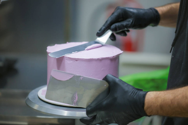 cukrász spatulával és kaparóval simító réteges lila vajkrém cukormázas torta - esküvői torta elkészítése - Fotó, kép