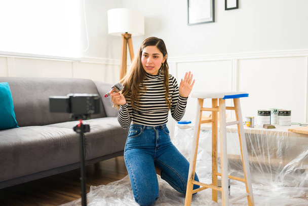 Atraktivní žena mluví při natáčení video tutorial pro sociální média při malování nábytku pro její DIY obchodní projekt - Fotografie, Obrázek
