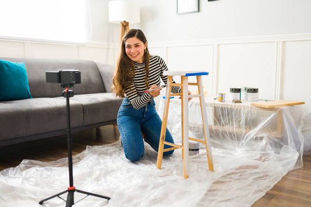 Onnellinen nainen hymyilee kuvaamisen video hänen älypuhelin tehdessään huonekalut flipping työtä ja maalaus jakkara - Valokuva, kuva