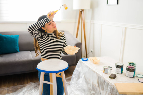 Zmęczona kobieta wyglądająca na wyczerpaną podczas malowania krzesła podczas pracy nad przerzucaniem mebli - Zdjęcie, obraz