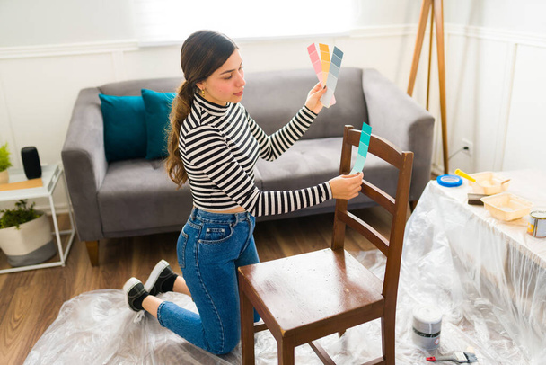 Latynoska kobieta wybiera kolor do malowania krzesła podczas naprawy mebli w domu - Zdjęcie, obraz