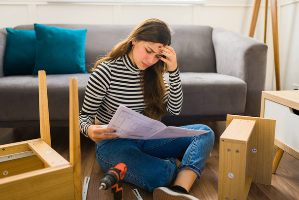 Mujer estresada sintiéndose molesta mientras lee las difíciles instrucciones para ensamblar muebles  - Foto, Imagen