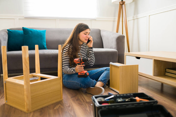 Droevige jonge vrouw op zoek gestresst praten aan de telefoon om hulp te vragen bij het monteren van moeilijke meubels - Foto, afbeelding