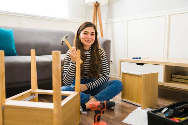Donna allegra sorridente che tiene un martello mentre fa e assembla nuovi mobili - Foto, immagini