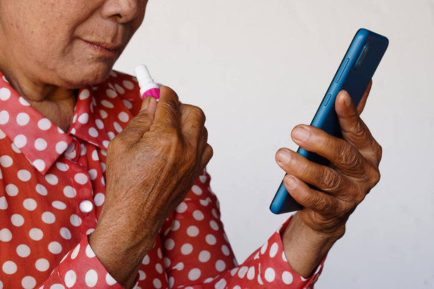 Старша жінка Клозап тримає тайський медичний інгалятор, щоб відчувати запах під час читання новин на смартфоні. Концепція, почуття і емоції, погані новини в Інтернеті. Старенькі та інтернет-технології в повсякденному житті.    - Фото, зображення
