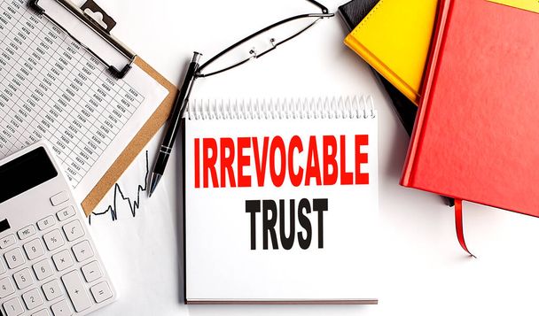 IRREVOCABLE TRUST text on notebook with clipboard and calculator on a white background - Photo, Image