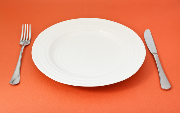 пустая белая тарелка с вилкой и ножом на красном
 - Фото, изображение