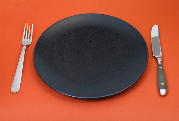 пустая черная тарелка с вилкой и ножом на красном
 - Фото, изображение