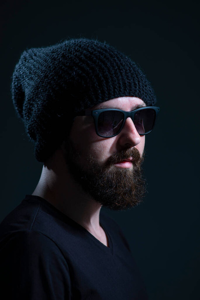Güneş gözlüklü sakallı bir milenyumun özgün portresi ve siyah örülmüş bir şapka.. - Fotoğraf, Görsel